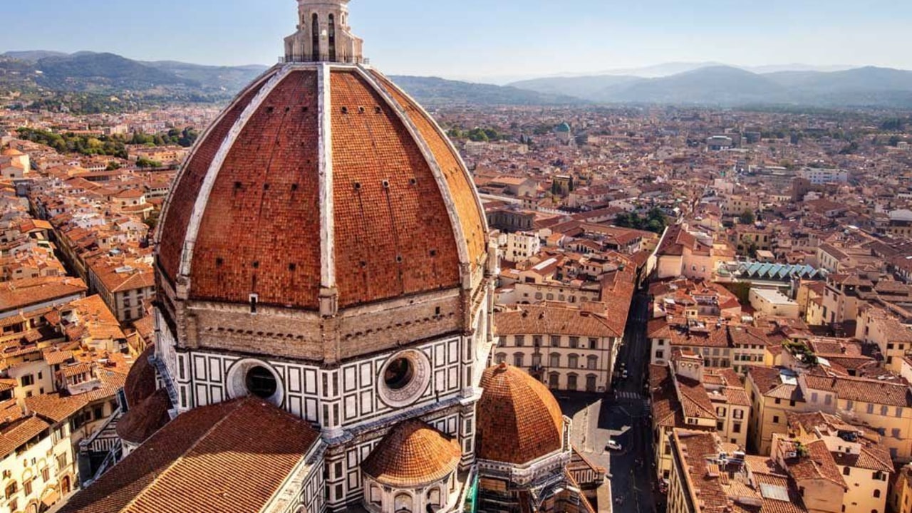 Aerial view of Brunelleschi's Dome atop Florence Cathedral, with the city's iconic terracotta rooftops and Tuscan hills stretching into the background.